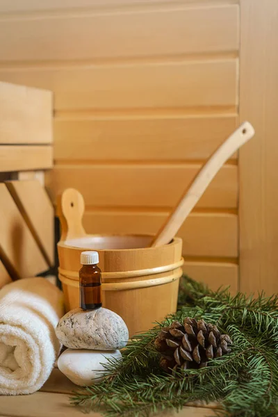 Spa, Finnish sauna and wellness setting with water bucket, oil essence, cones, Christmas tree branches, white towel on wooden background. autumn winter wellness concept relax and treatment therapy.