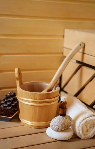 small private Finnish sauna setting with water bucket, oil essence, cones, hot stones and white towel on wooden background. wellness spa concept relax and treatment therapy. Selective focus, close up
