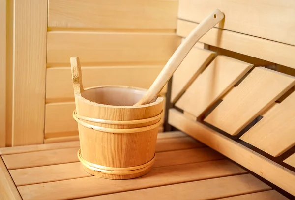 Small private Finnish sauna setting with water bucket, oil essence, cones, hot stones and white towel on wooden background. wellness spa concept relax and treatment therapy. Selective focus, close up — Stock Photo, Image