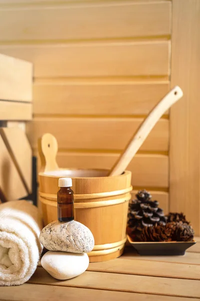 small private Finnish sauna setting with water bucket, oil essence, cones, hot stones and white towel on wooden background. wellness spa concept relax and treatment therapy. Selective focus, close up