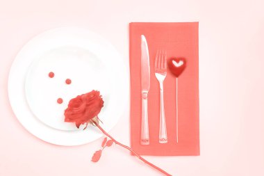 Üstten görünüm romantik tablo ayarı için Sevgililer günü ya da akşam yemeği tarihi düğün kutlama kırmızı pastel mercan renk arka plan üzerinde mercan masa örtüsü üzerinde bud Beyaz tabaklar çatal ve bıçak gül.