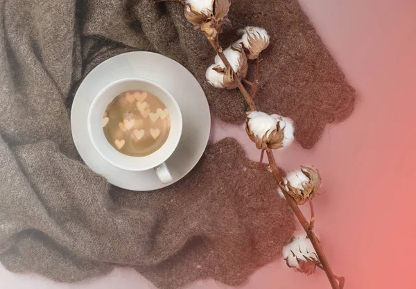 Russian woolen shawl with cup of coffee with hearts inside and cotton branch on color of the year 2019 Living Coral background. Romantic winter concept for blogger. Top view, copy space.