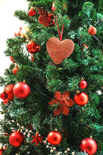 Red textile heart hanging on fir branch, fir tree decorated red balls. Merry Christmas, Happy New Year and Valentines Day greeting concept. Stock Picture