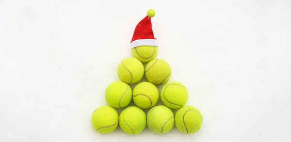 Tenis topu beyaz kar arka plan üzerinde Santa şapka. Noel ve yeni yıl konseptiyle tenis topları. Sarı yeşil renkli tenis topları şekil köknar ağacı. Yakın çekim, spor yaşam tarzı