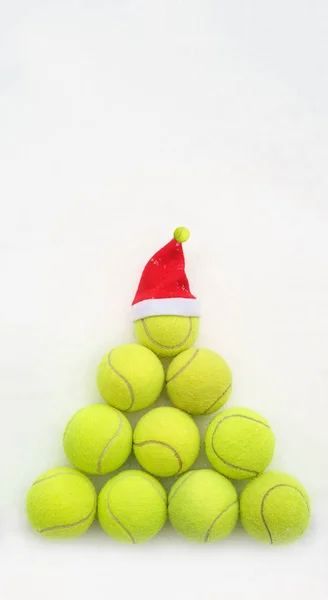 Tenis topu beyaz kar arka plan üzerinde Santa şapka. Noel ve yeni yıl konseptiyle tenis topları. Sarı yeşil renkli tenis topları şekil köknar ağacı. Yakın çekim, spor yaşam tarzı