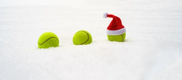 Santa hat na piłkę tenisową na tle białego śniegu. Boże Narodzenie i nowy rok koncepcja z piłek tenisowych. Zbliżenie, sport styl życia — Zdjęcie stockowe