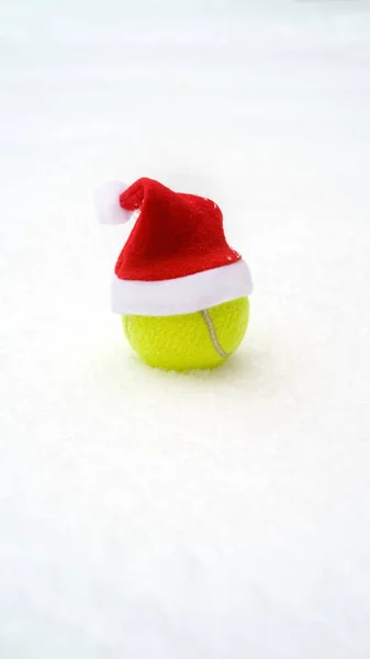 Santa hat on tennis ball on white snow background. Christmas and New year concept with tennis balls. Close up, sport lifestyle