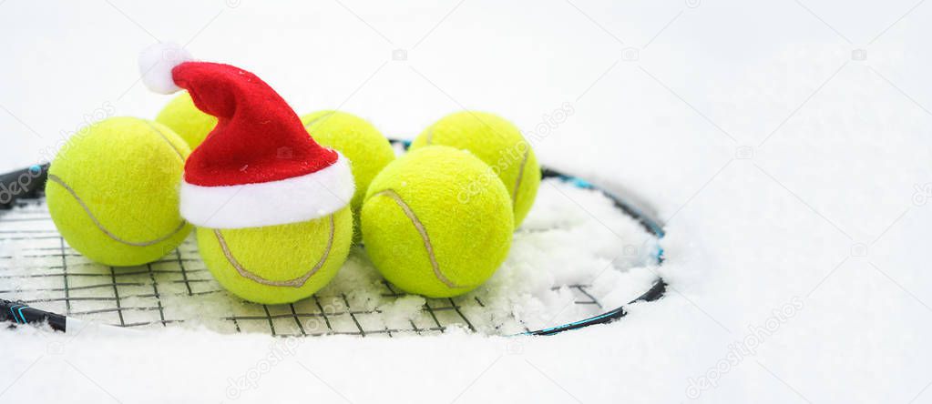 Santa hat on tennis ball, set of tennis balls on racket on white snow winter background. Merry Christmas and New year concept with tennis balls play. Close up, sport lifestyle, funny.