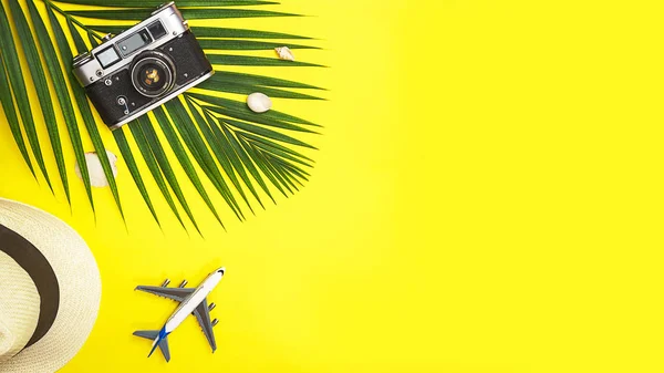 Flat lay acessórios para viajantes folha de palma tropical, chapéu de palha branco, brinquedo avião, câmera retro e conchas no fundo colorido amarelo com espaço para texto. Viagens férias verão conceito. vista superior — Fotografia de Stock