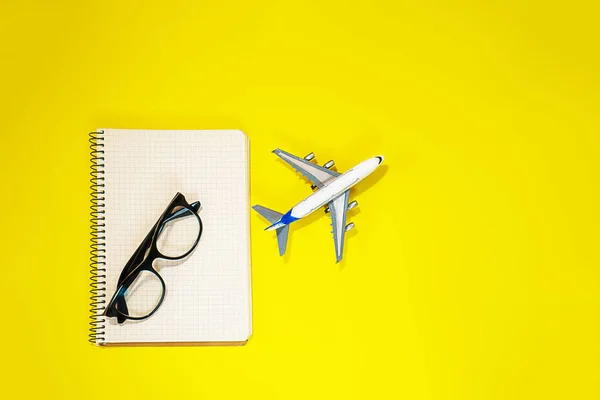 Layout mínimo com avião modelo, caderno em espiral e óculos de moda em fundo amarelo. Diretamente acima. Viagens férias verão conceito. leigos planos, composição vista superior . — Fotografia de Stock