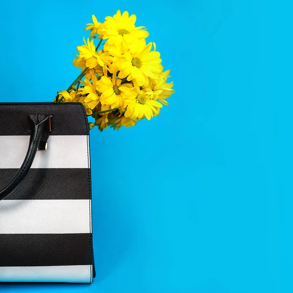 Female business accessories: black and white bag yellow flowers on blue background.