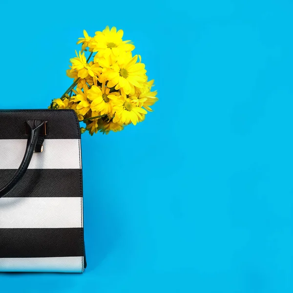 Krásné žluté květy a černé a bílé módní dámské kabelky na modrém pozadí. — Stock fotografie