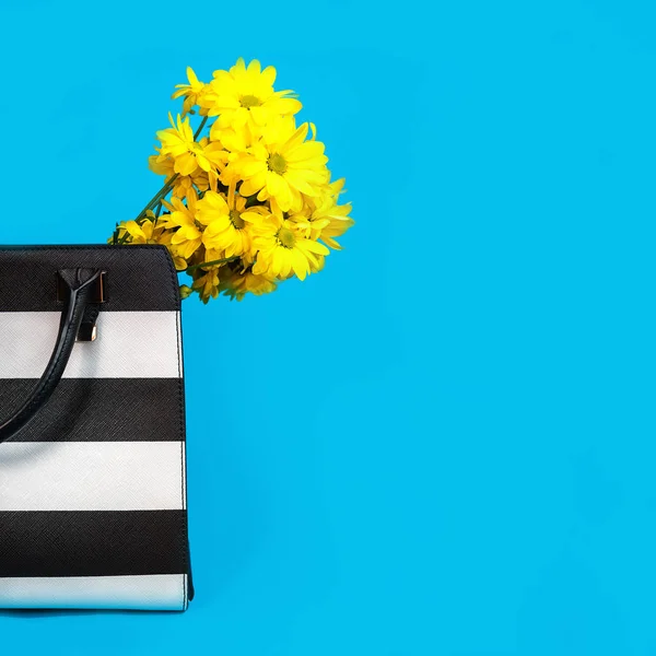 Vackra gula blommor och svartvita trendig kvinnliga väska på blå bakgrund. — Stockfoto