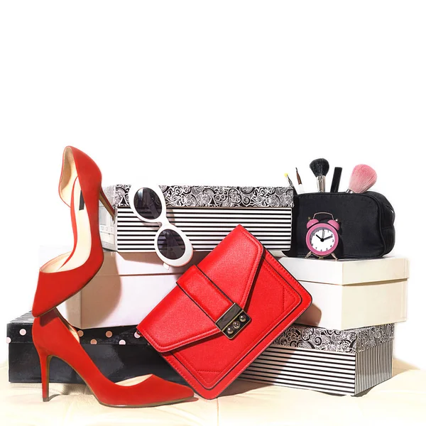 Composición del conjunto de fiesta vista superior: zapatos rojos de accesorios femeninos de moda, gafas de sol de embrague de bolso, cosméticos, maquillaje, reloj despertador para fiesta en cajas de cartón sobre fondo blanco . —  Fotos de Stock