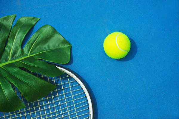 Sommar tennis koncept med gröna monstera löv och boll, Racquet på hård tennisbana. — Stockfoto