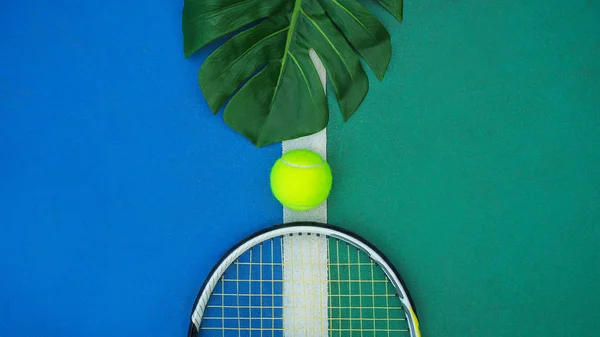 Summer sport concept with green monstera leaf and tennis ball, racquet on white line on hard tennis court. — Stock Photo, Image