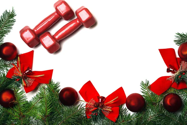 Спорт Різдвяний та новорічний фон з червоними гантелями, зеленими гілками ялинки червоні скляні кульки та червоні луки дзвони на білому тлі . — стокове фото