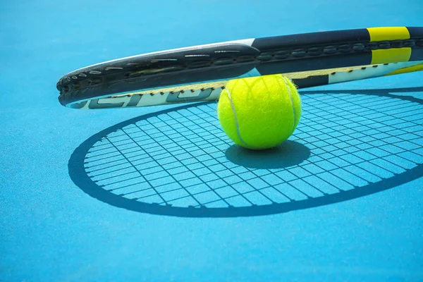 Summer sport concept with tennis ball and racket on blue hard tennis court.