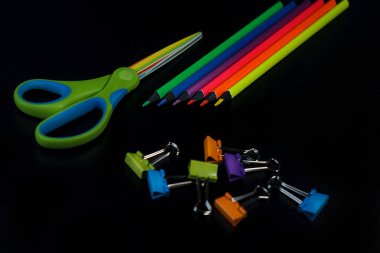 Kalemler, makaslar, siyah zemin üzerinde renkli ataşile okul arka planına geri dön.