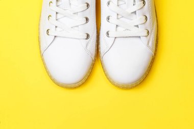 Beyaz spor ayakkabıları pastel sarı arka planda yatıyor.