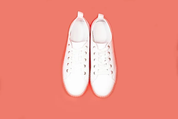 White sneakers are lying on a pastel pink coral background. — Stock Photo, Image