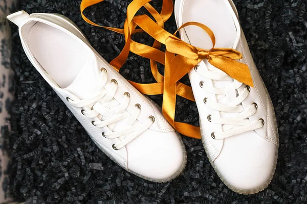 White sneakers and yellow bow are lying on textured black box background. — Stock Photo, Image