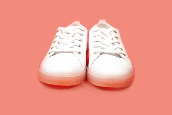 White sneakers are lying on a pastel pink coral background. — Stock Photo, Image
