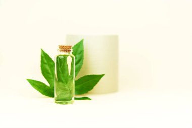 Bitkisel CBD yağlı cam şişe, bej arka planda tentür ve kenevir yaprağı.