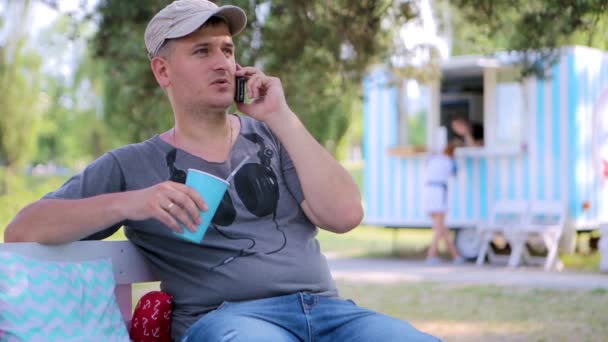 男人在公园里的电话里用柠檬水在长椅上聊天 — 图库视频影像
