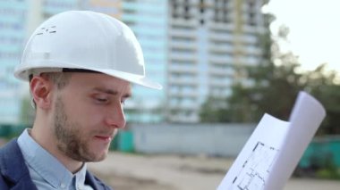Yakın plan, beyaz kasklı bir mühendis elinde inşaat çizimleri tutuyor.