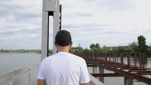 一个年轻人走在一座狭窄的桥上 回头看相机 — 图库视频影像