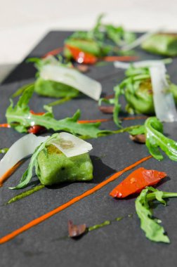 Zengin yeşil ıspanak polenta, dilimlenmiş zeytin, roket, biber, servis güneş kurutulmuş domates ve ince parmesan dilimleri. Tabakta çağdaş bir kayrak.