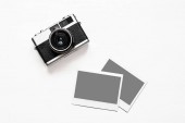 Flatlay vinobraní retro fotoaparát na dřevěné bílé pozadí s prázdný papír instantní fotografie umístěny obrázky. Pohled shora