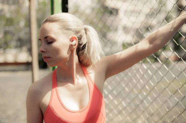 Fitness-Frau hört Musik in drahtlosen Kopfhörern, macht Workout-Übungen auf der Straße. Bluetooth-Kopfhörer im Sport-Stil — Stockfoto