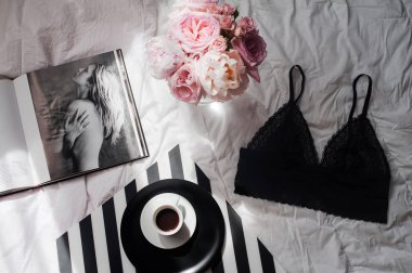 Düz lay, dergiler, sosyal medya. Üstten görünüm siyah dantel iç çamaşırı. Güzellik blog kavramı. Kadın moda aksesuarları, iç çamaşırı, buket gül ve pions, beyaz yatak zemin üzerine kahve