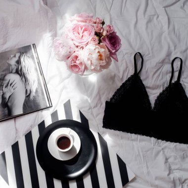Düz yatıyordu. Üstten görünüm siyah dantel iç çamaşırı. Güzellik blog kavramı. Buket gül ve pions, beyaz yatak arka plan üzerinde kahve