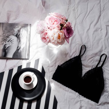 Düz yatıyordu. Üstten görünüm siyah dantel iç çamaşırı. Güzellik blog kavramı. Buket gül ve pions, beyaz yatak arka plan üzerinde kahve