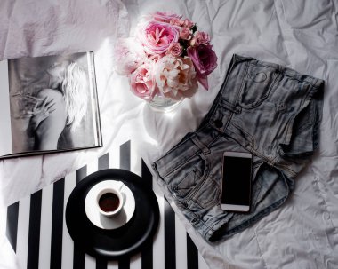 Düz lay, dergiler, sosyal medya. Üstten görünüm. Güzellik blog kavramı. Kadın moda aksesuarları, şort, buket gül ve pions, telefon ve kahve beyaz yatak zemin üzerine