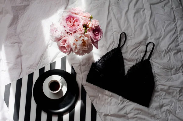 플랫이 하다. 상위 뷰 블랙 레이스 란제리입니다. 뷰티 블로그 개념입니다. 장미와 pions, 흰색 침대 배경에 커피의 꽃다발 — 스톡 사진