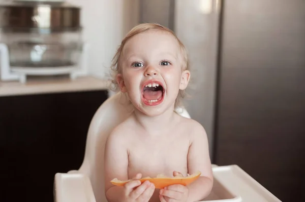 小女孩吃哈密瓜。有趣的笑孩子在厨房里。愉快的孩子在高椅子 — 图库照片