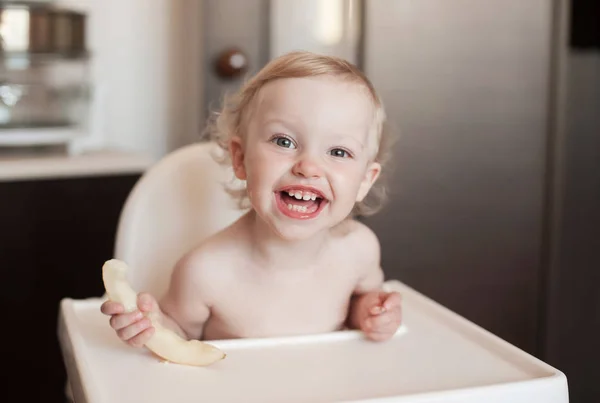 Bebé comiendo melón melón. Gracioso niño riendo en la cocina. Alegre niño en la silla alta —  Fotos de Stock