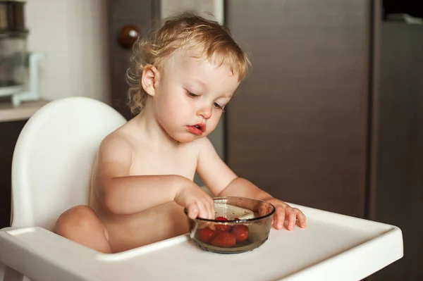 Eszik szamóca kislány. Vicces nevető gyermek a konyhában. Vidám gyerek a etetőszék — Stock Fotó