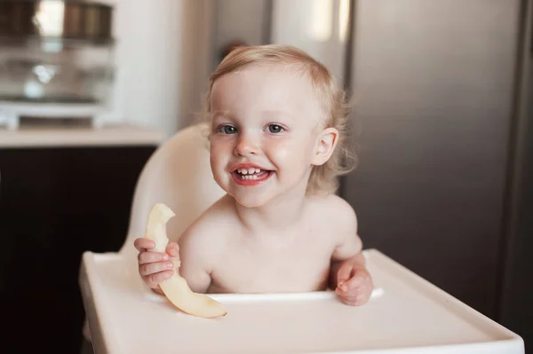 Bebé comiendo melón melón. Gracioso niño riendo en la cocina. Alegre niño en la silla alta —  Fotos de Stock