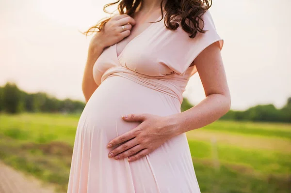 Barriga de uma mulher grávida ao pôr-do-sol. Menina grávida sentindo o bebê . — Fotografia de Stock