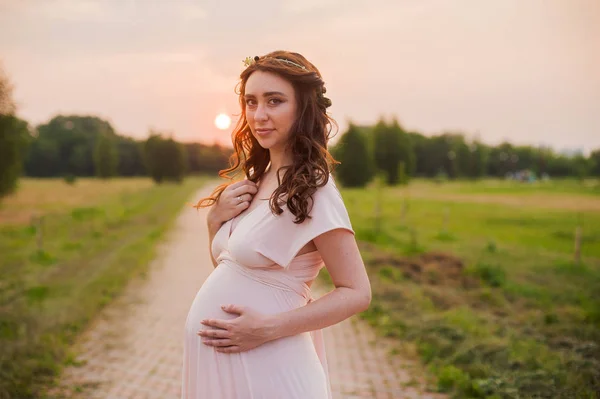 Retrato de una mujer embarazada feliz en un parque al amanecer con una cálida luz de fondo rosa —  Fotos de Stock
