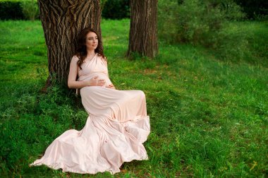 Hamile kadın 25-29 yaşındaki göl kenarında oturan gülümsüyor. Açık havada poz. Annelik. Annelik.