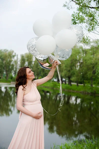 Feliz bela mulher grávida em vestido longo rosa andando com balões de ar no parque verde no dia de verão . — Fotografia de Stock
