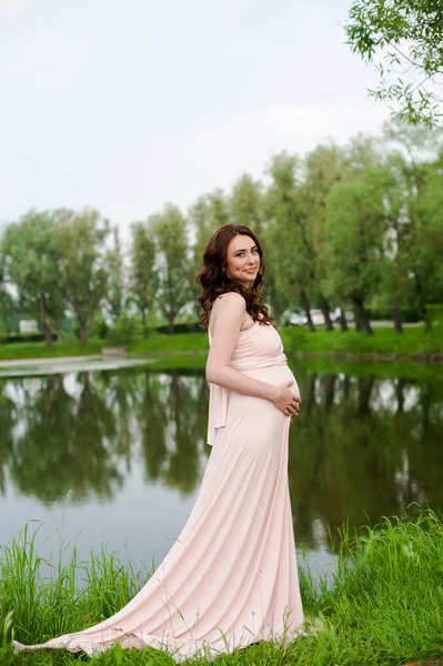 Smiling pregnant woman 25-29 year old resting by the lake. Posing outdoors. Motherhood. Maternity. Royalty Free Stock Photos