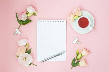 Kadınsı office çalışma alanı. Defter ile boşaltmak. Düz yatıyordu, sosyal medya, üstten görünüm. Pembe çiçekler, pastel pembe bir arka plan üzerinde çay.