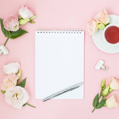 Kadınsı office çalışma alanı. Defter ile boşaltmak. Düz yatıyordu, sosyal medya, üstten görünüm. Pembe çiçekler, pastel pembe bir arka plan üzerinde çay.